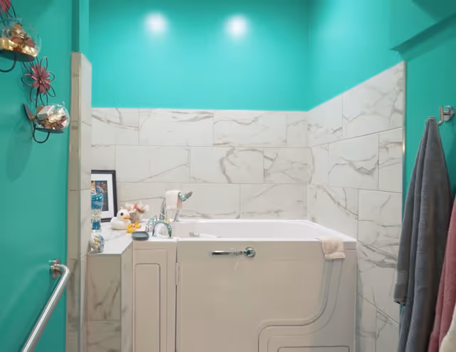 Bright teal bathroom with marble-tiled walls and a white washing machine.