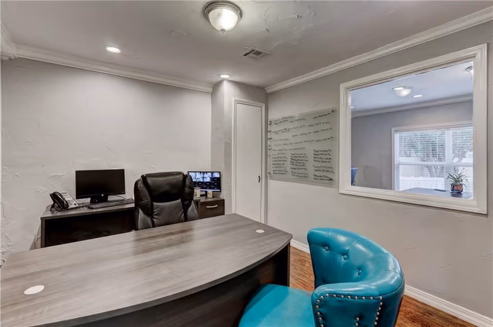 Office desk with computer, phone, and a teal chair in a small office.
