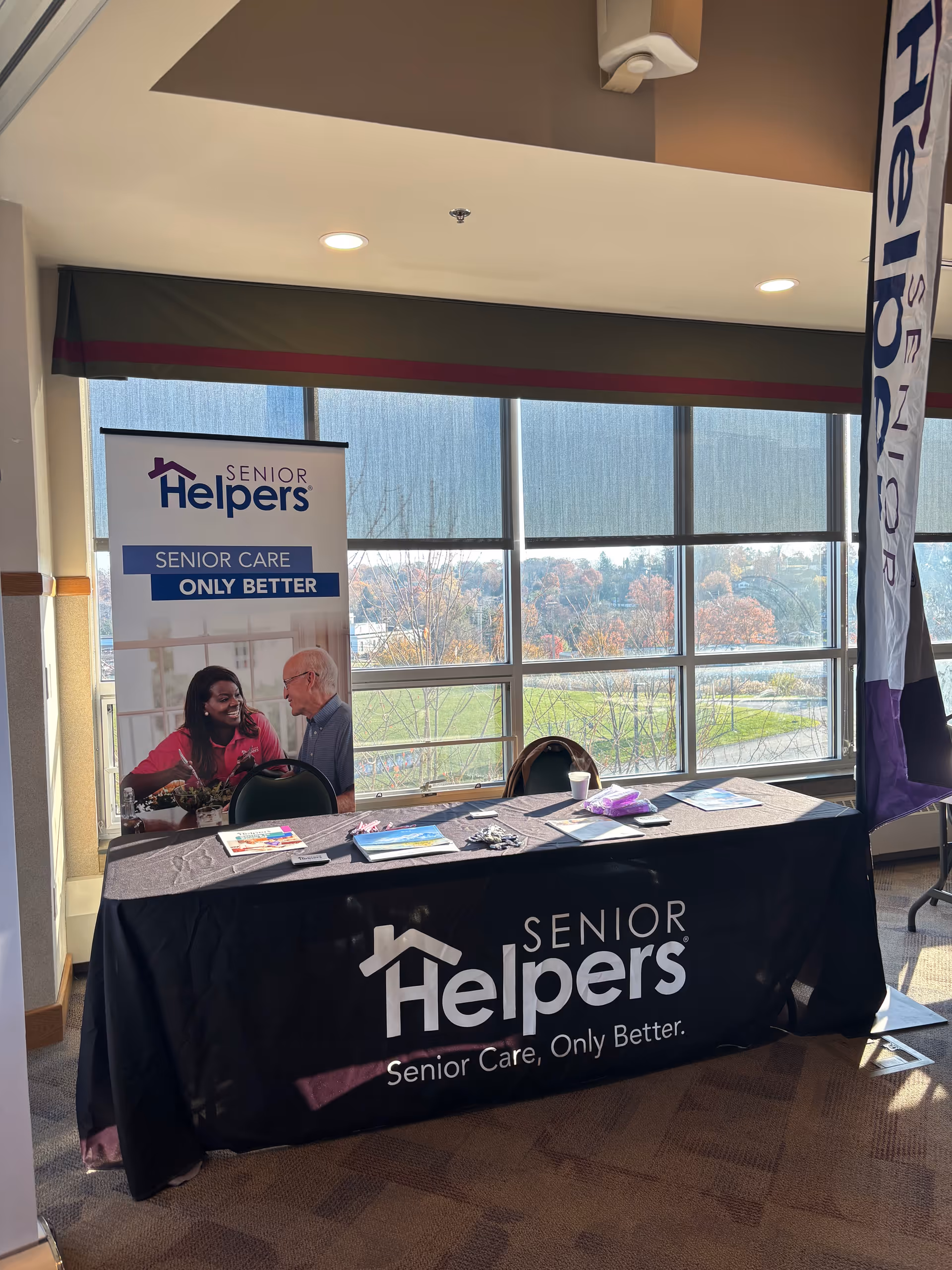 An information table for Senior Helpers sits in a bright lobby with banners and brochures.