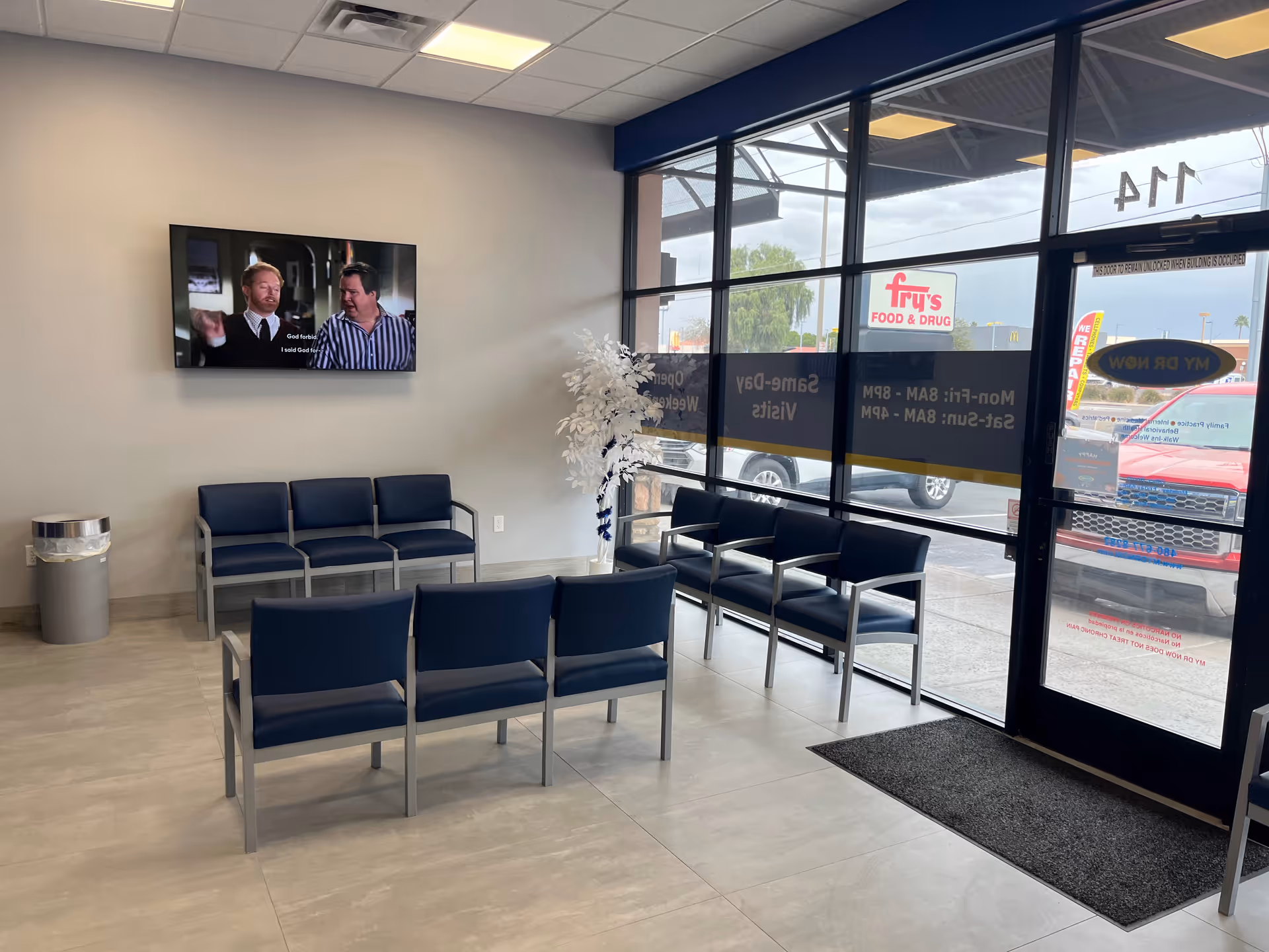 Lobby waiting area with blue chairs, mounted TV, and large glass windows.