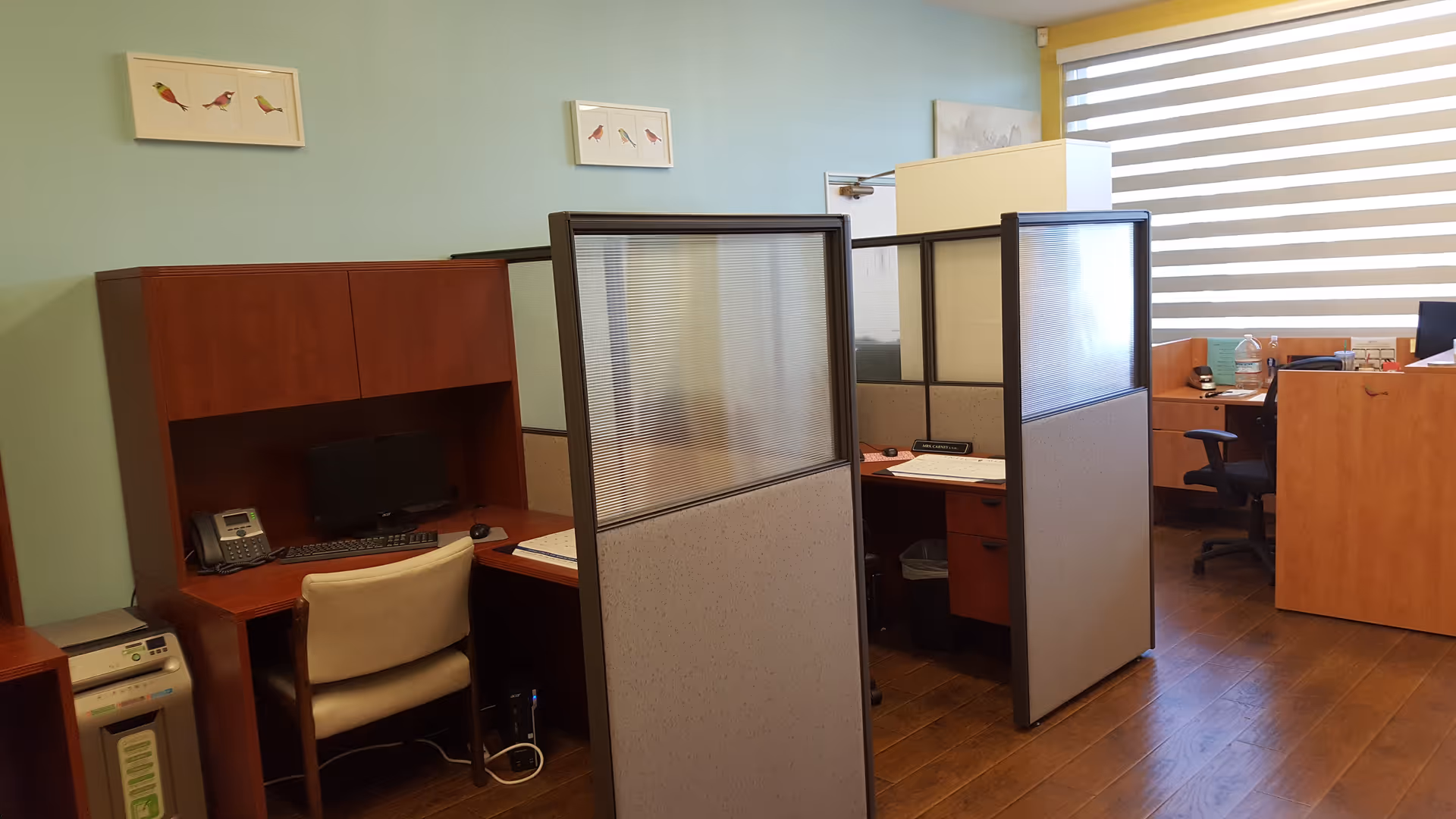 Office cubicles with computers and frosted partition panels inside a facility.
