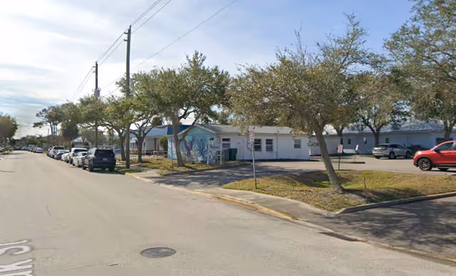Street view of a single-story Senior Helpers facility with trees, parked cars, and a mural.