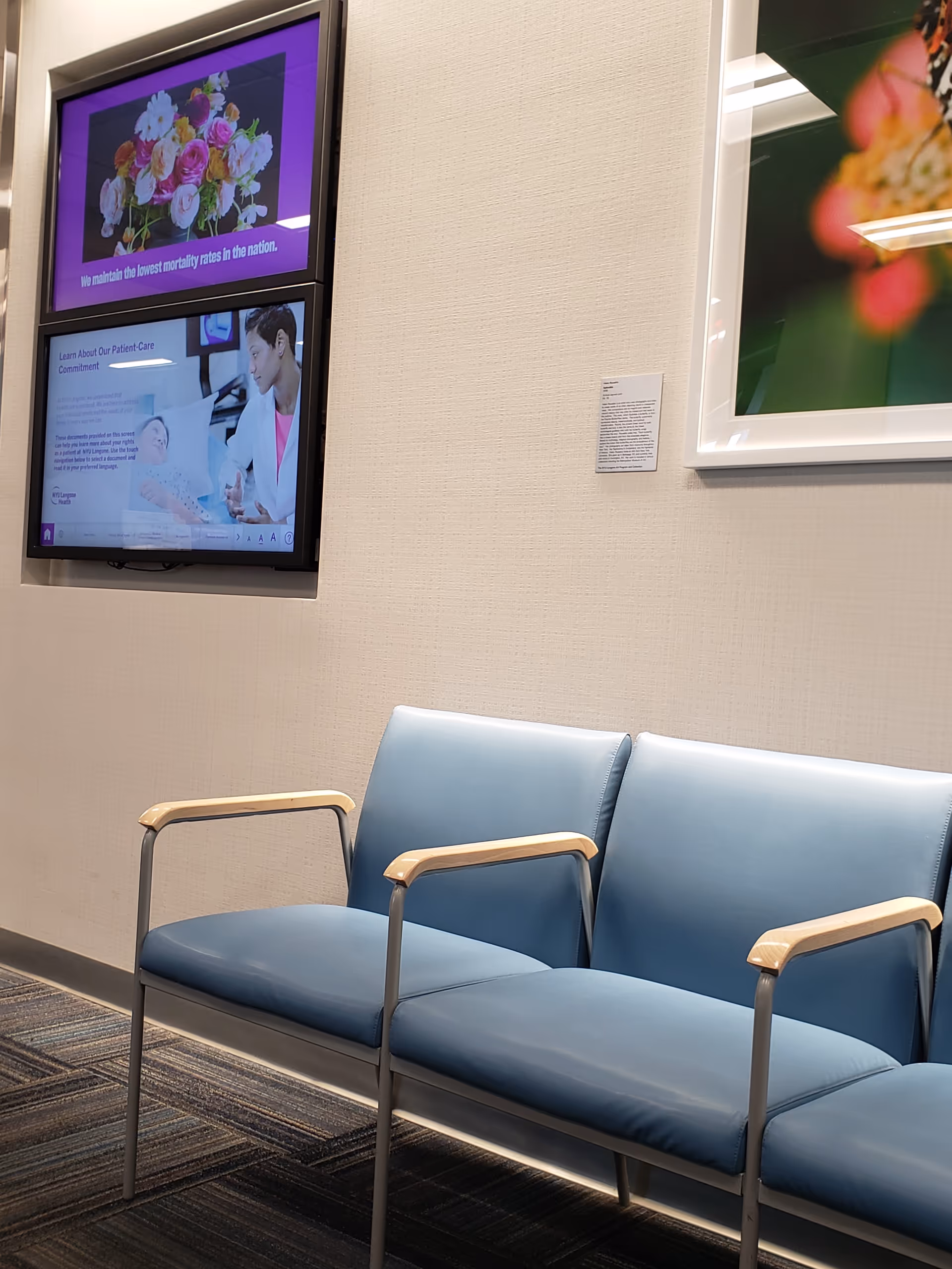 Waiting area with blue cushioned chairs along wall and posters on beige walls.