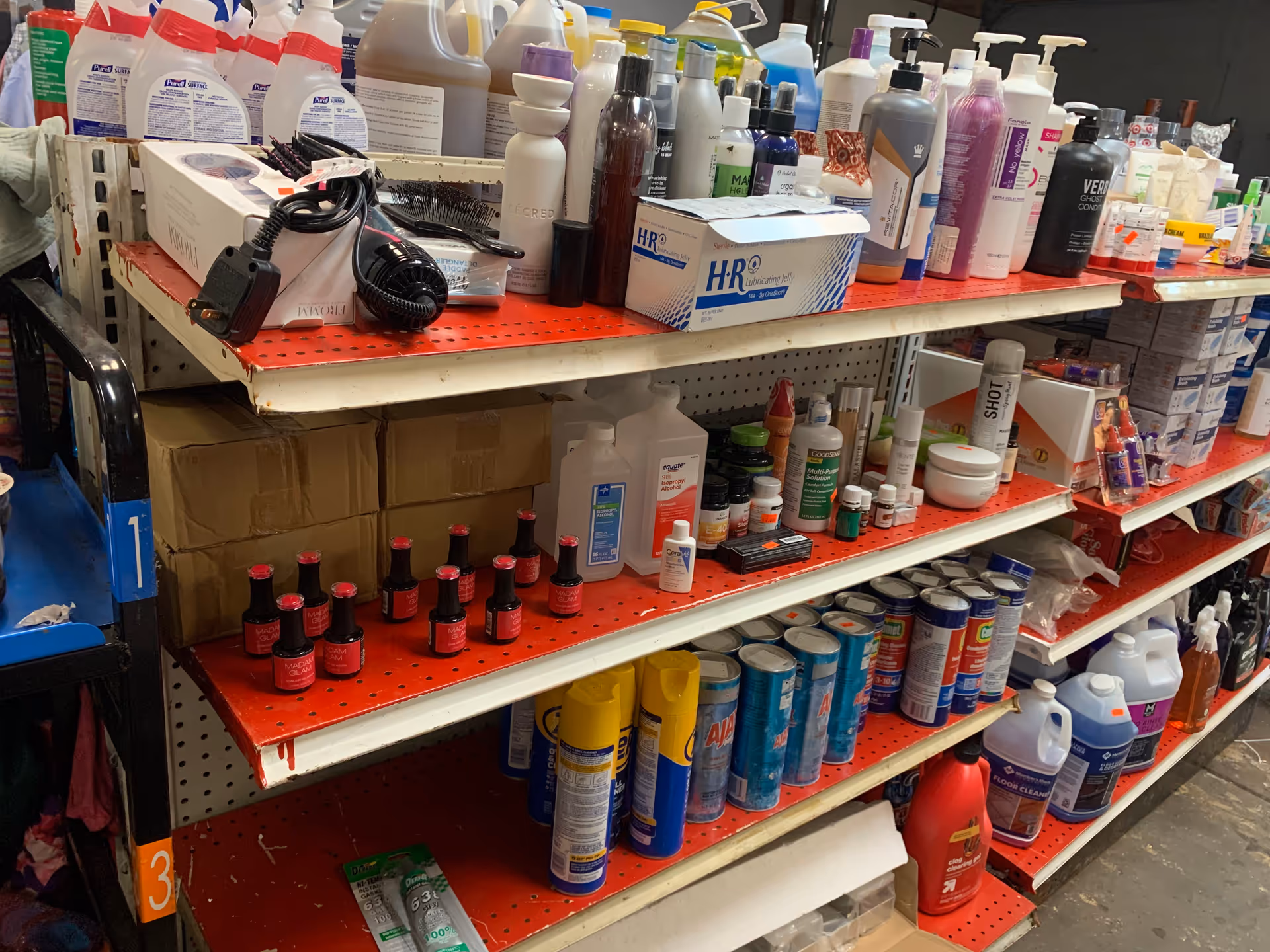 The image shows an aisle filled with cleaning products on red perforated shelves.