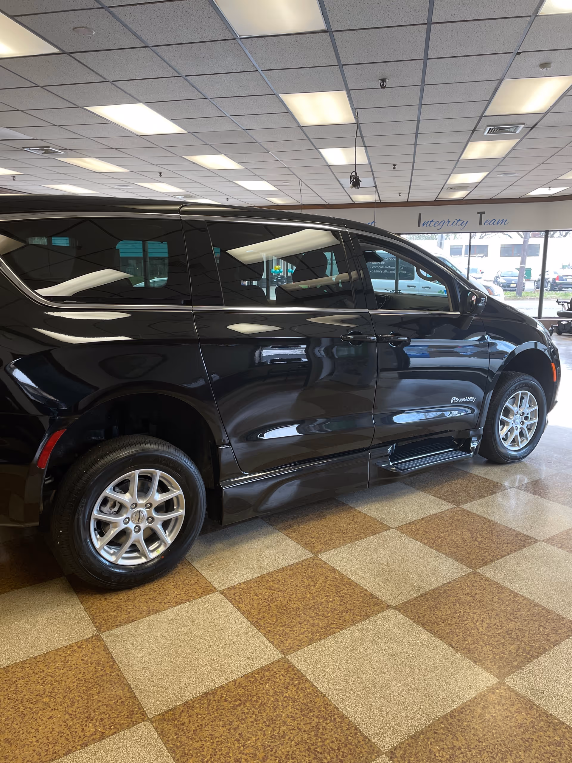 Inside a MobilityWorks showroom, a shiny black wheelchair-accessible van sits on a checkered tile floor.