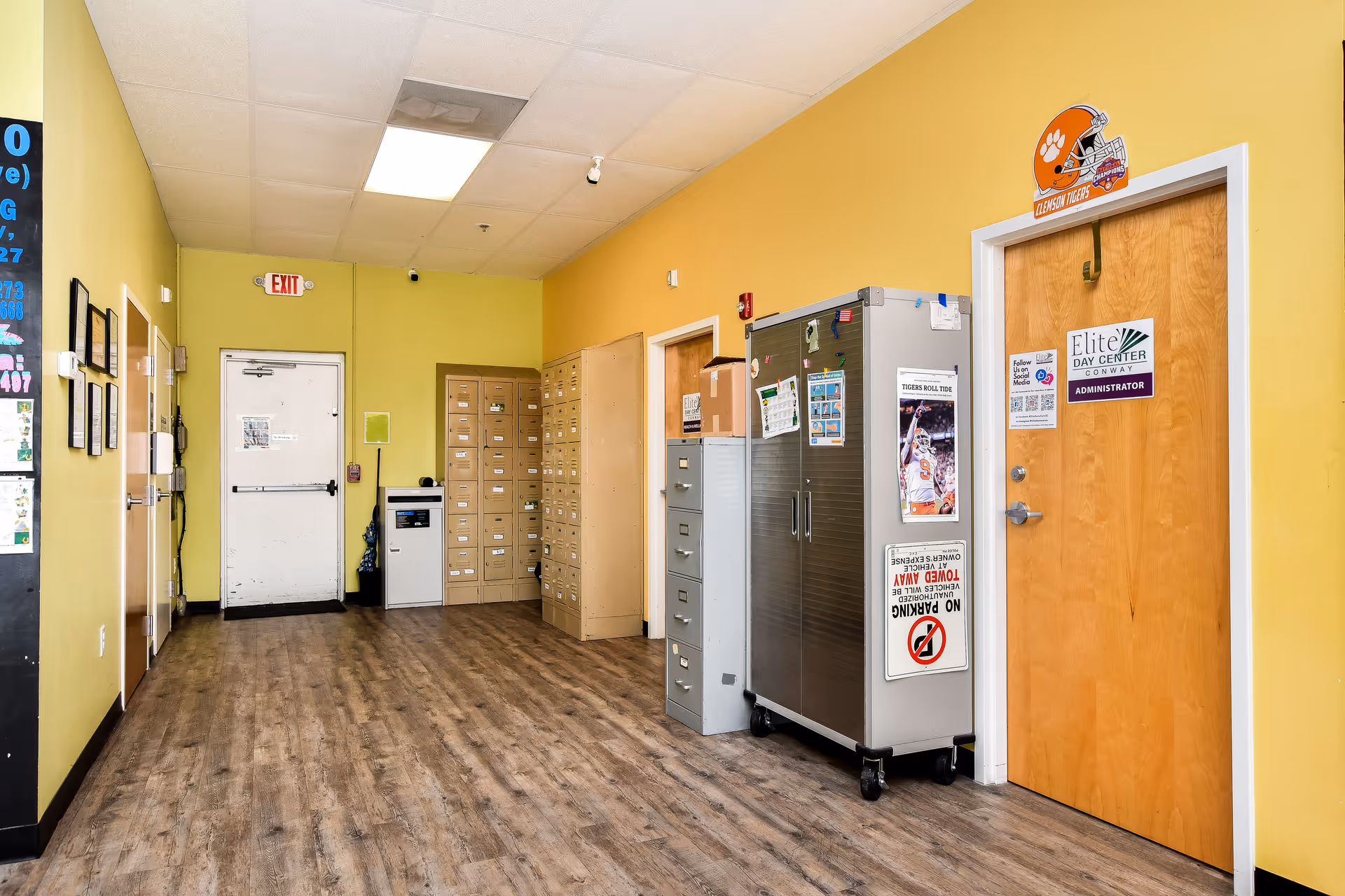 Yellow-walled hallway in a senior care facility with mailboxes, lockers, and labeled doors.