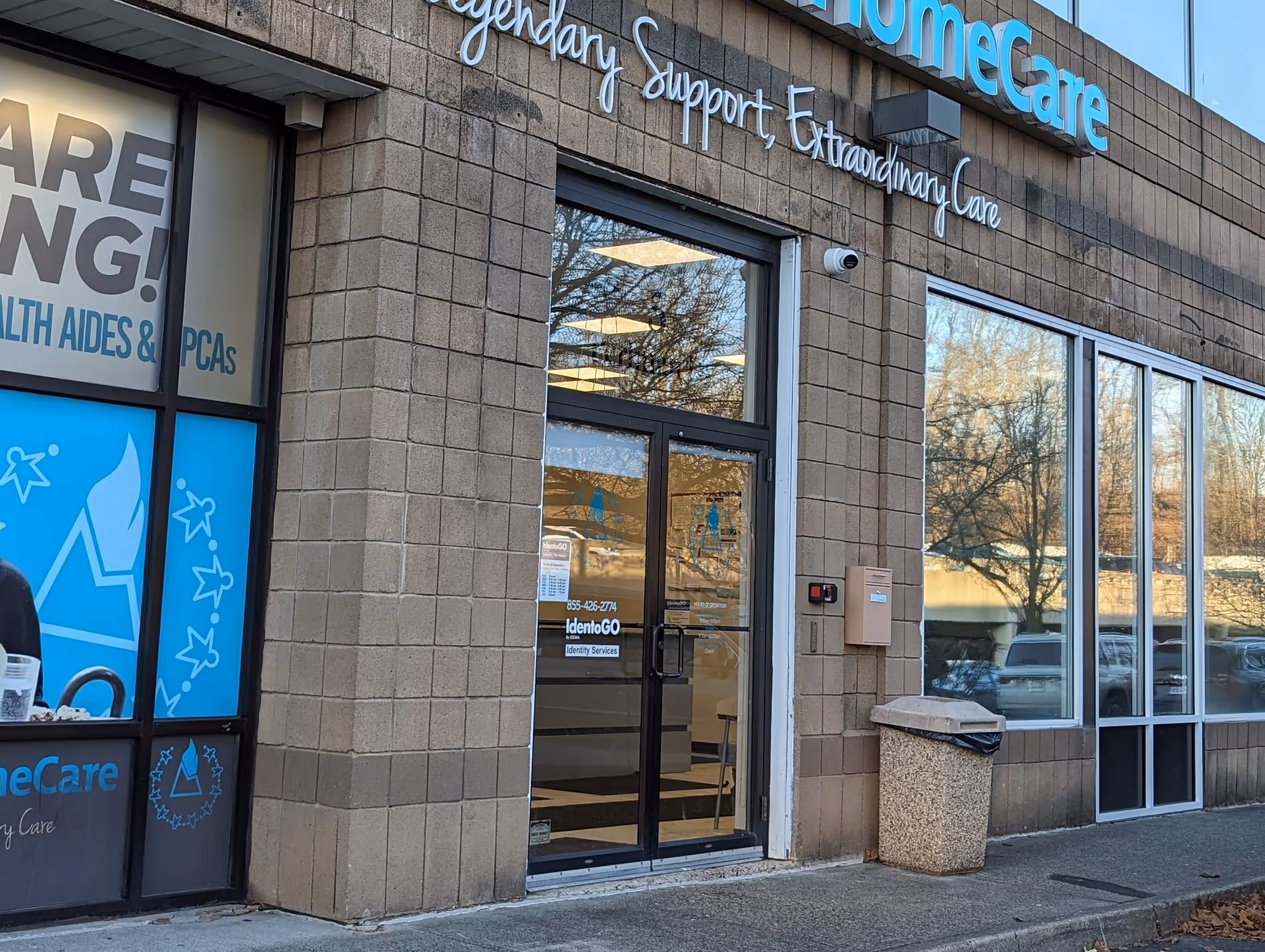 Exterior view of Hamaspik HomeCare entrance with glass doors, signage, and a trash bin outside.