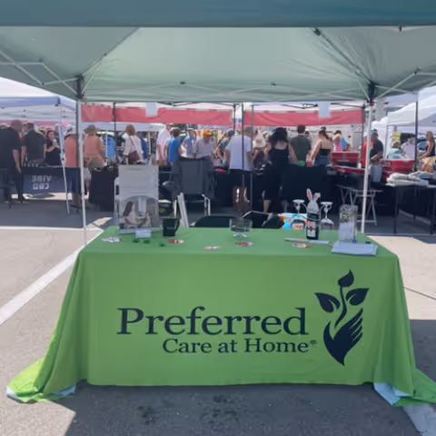 Outdoor market scene with a green tablecloth reading Preferred Care at Home under tents.