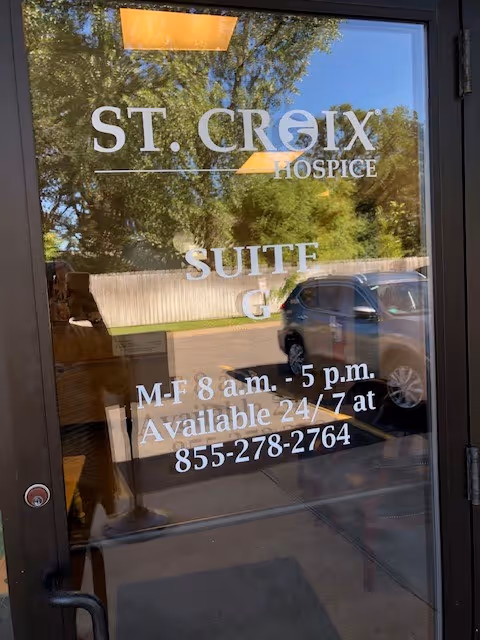 Glass door with St. Croix Hospice sign and reflection of car and trees outside.