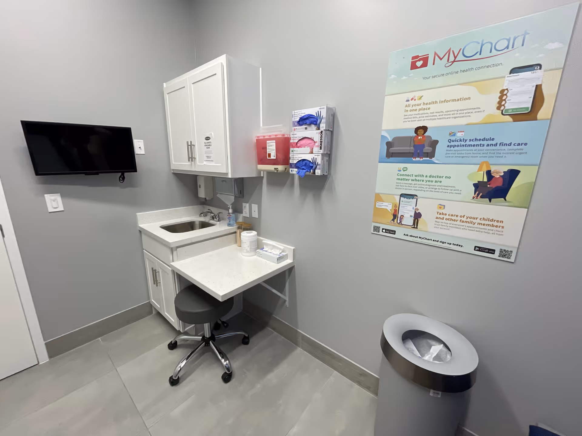 This is a small medical station with sink, cabinets, a stool, monitor, and a MyChart poster.