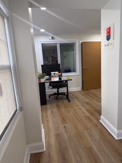 A hallway interior with a small desk, computer, and plants near a doorway.