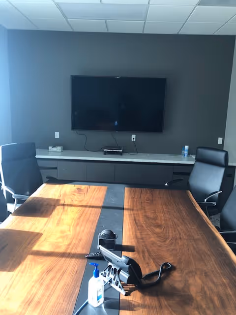 Interior conference room with a wall-mounted TV and a large wooden table.