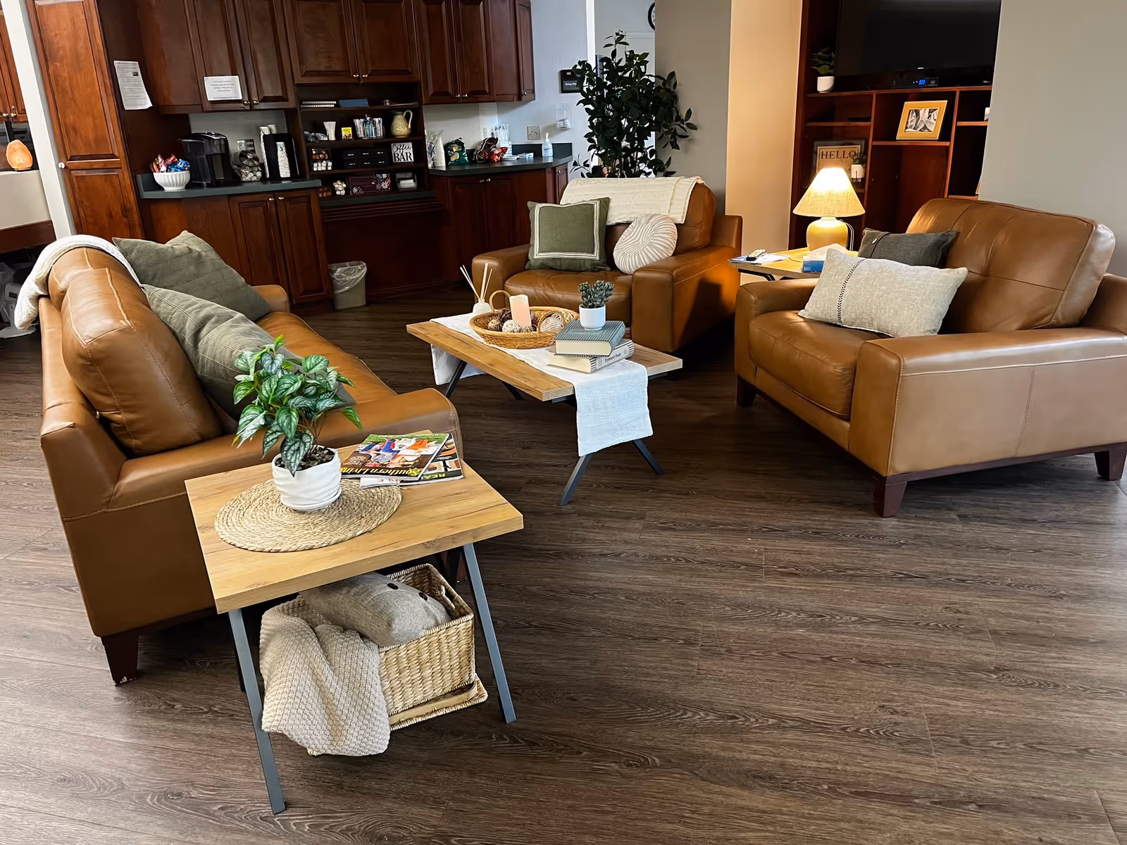 Brown leather seating area with wooden coffee tables and a kitchenette in a cozy common lounge.