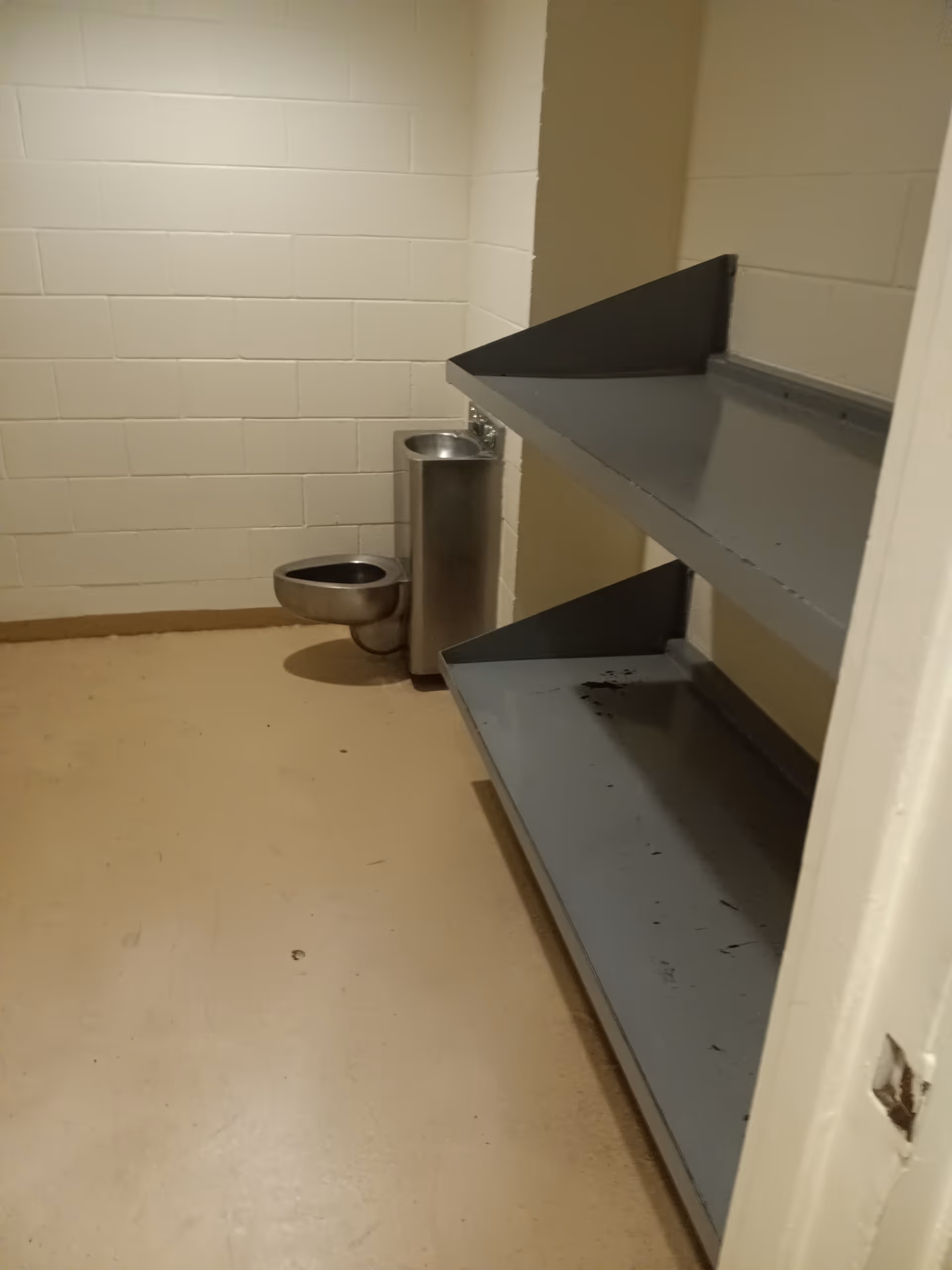 Small utility room with metal shelving, a trash can, and tiled white walls.