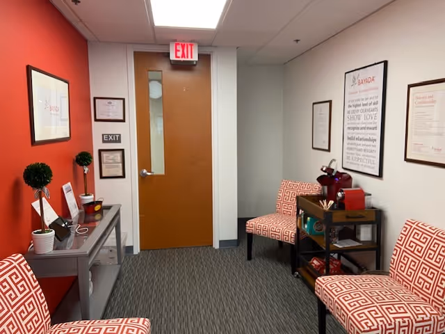 Interior hallway seating area with red walls, patterned chairs, and framed art.