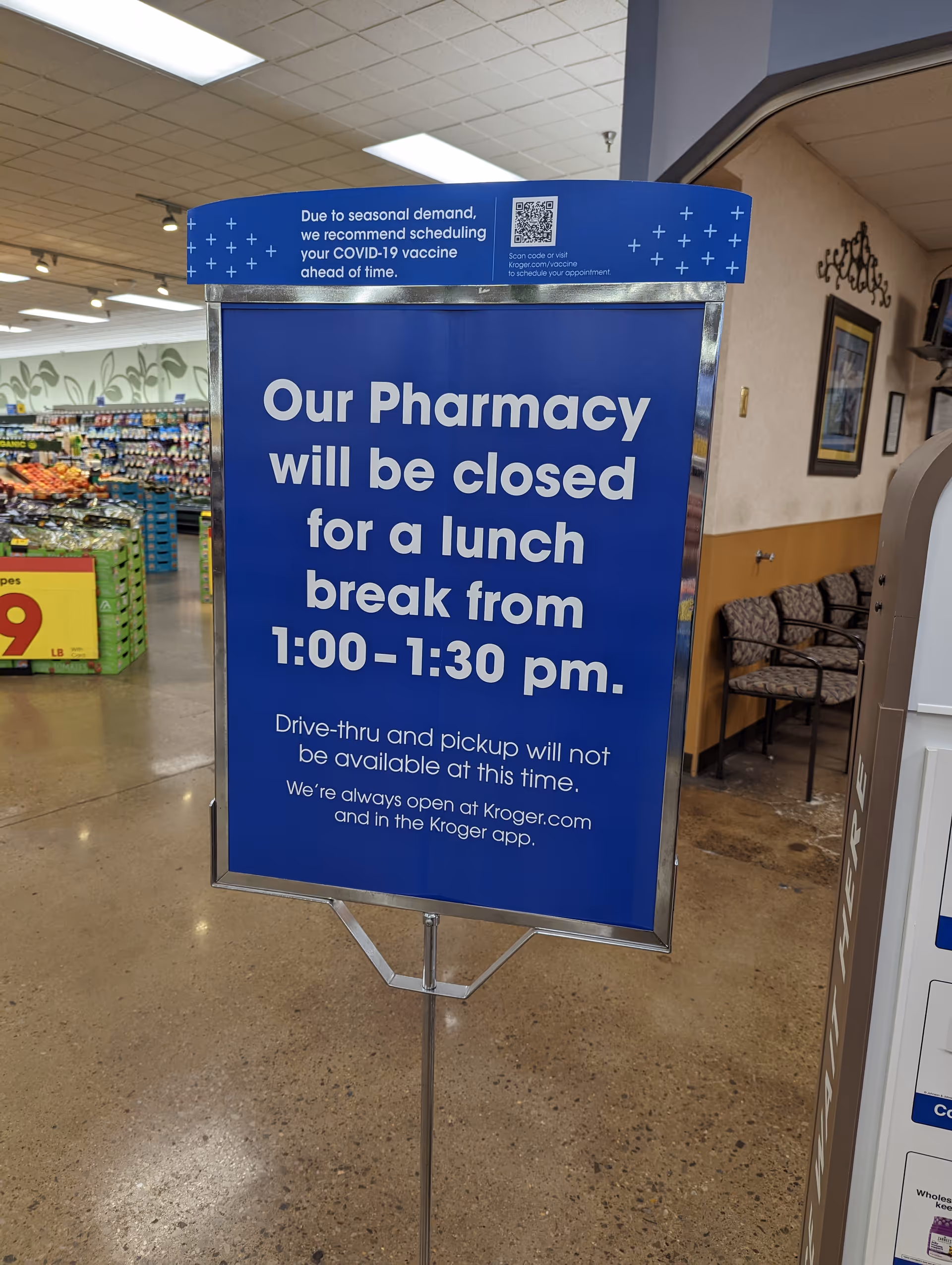 Blue Kroger Pharmacy sign informs lunch-break closure; grocery aisles visible nearby inside.