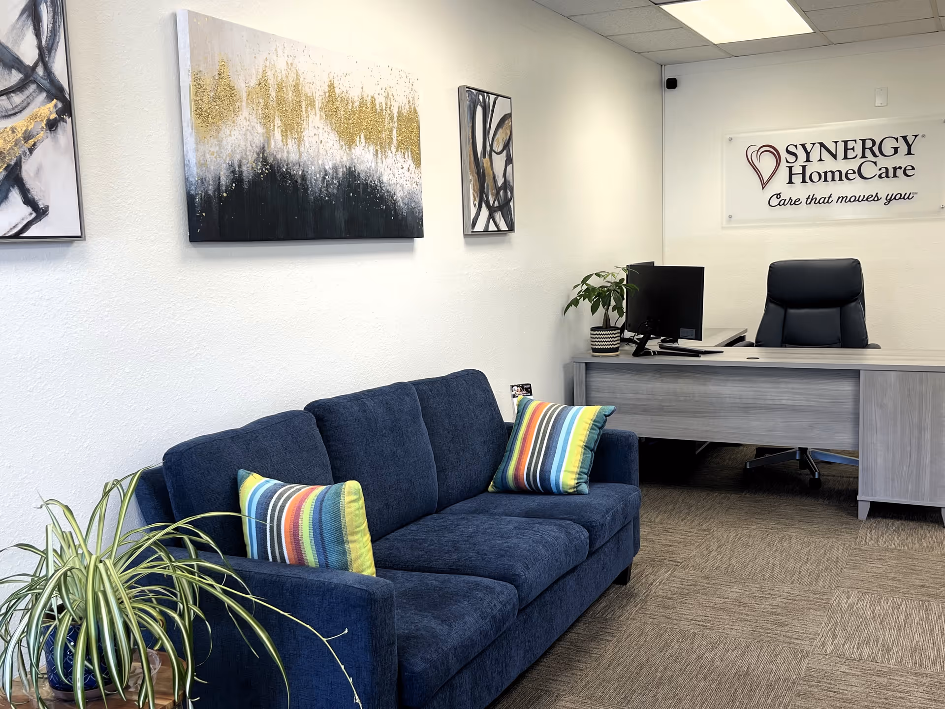 Reception area featuring a blue couch, desk, and Synergy HomeCare sign on the wall.