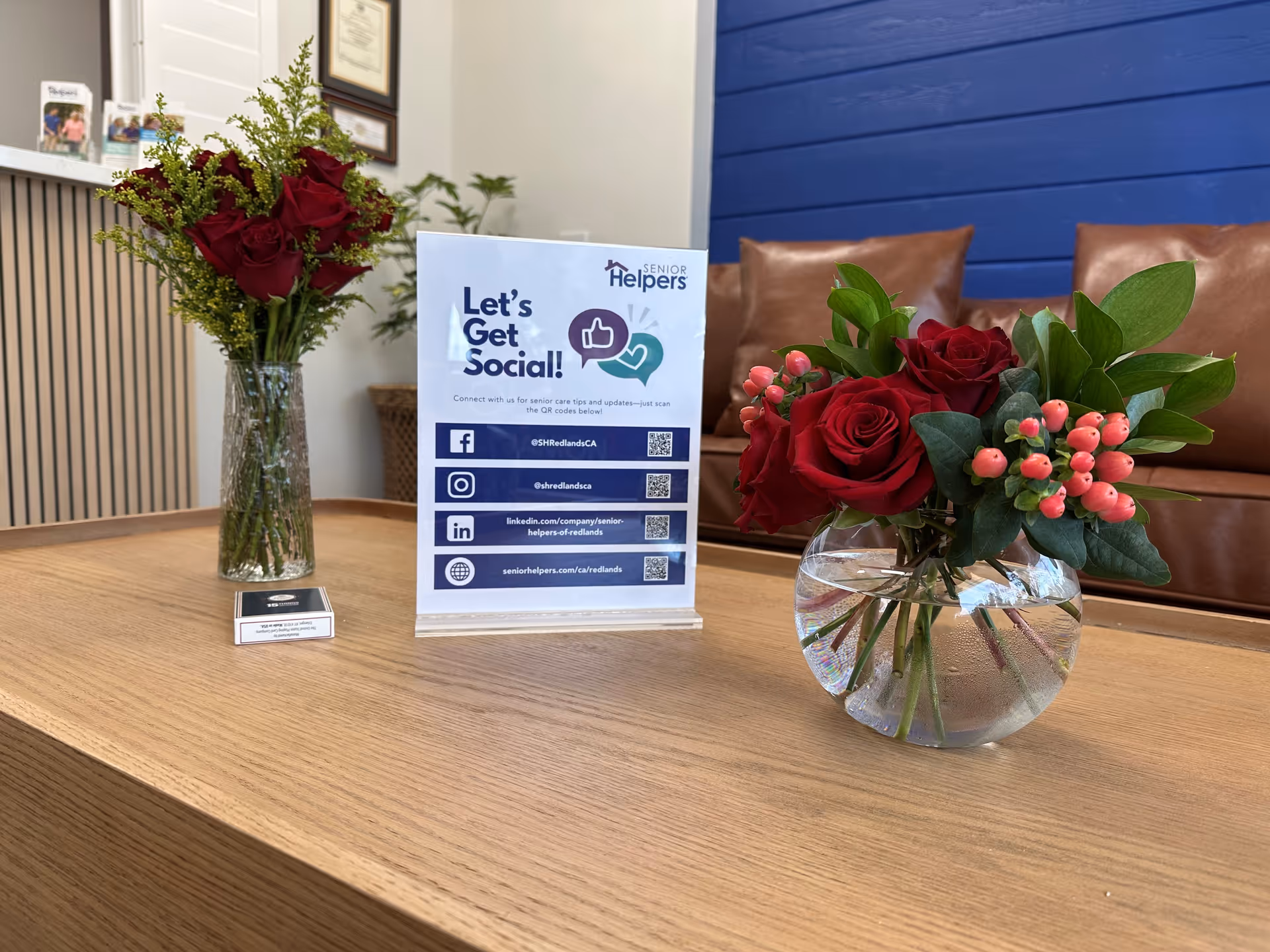 A lobby desk with flower arrangements and a 'Let's Get Social' sign for Senior Helpers.