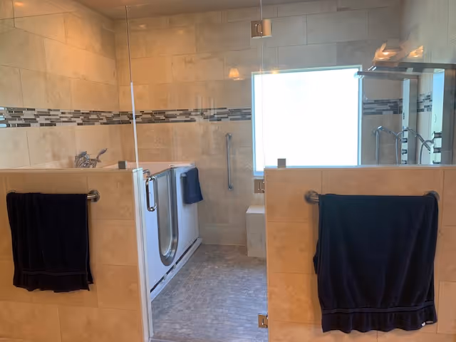 Spacious tiled bathroom featuring a walk-in tub, glass shower, and dark towels.