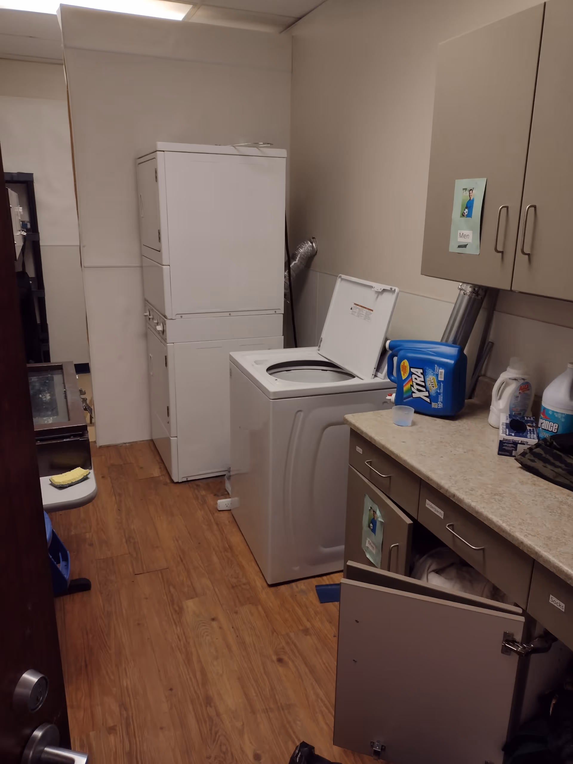 Small utility laundry room with stacked washer/dryer, cabinets, and cleaning supplies