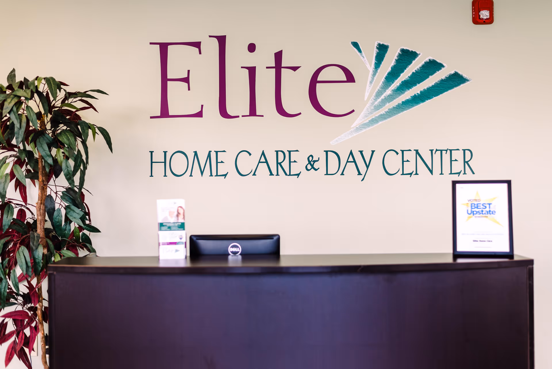 Reception desk in a lobby with Elite Home Care & Day Center logo on wall.