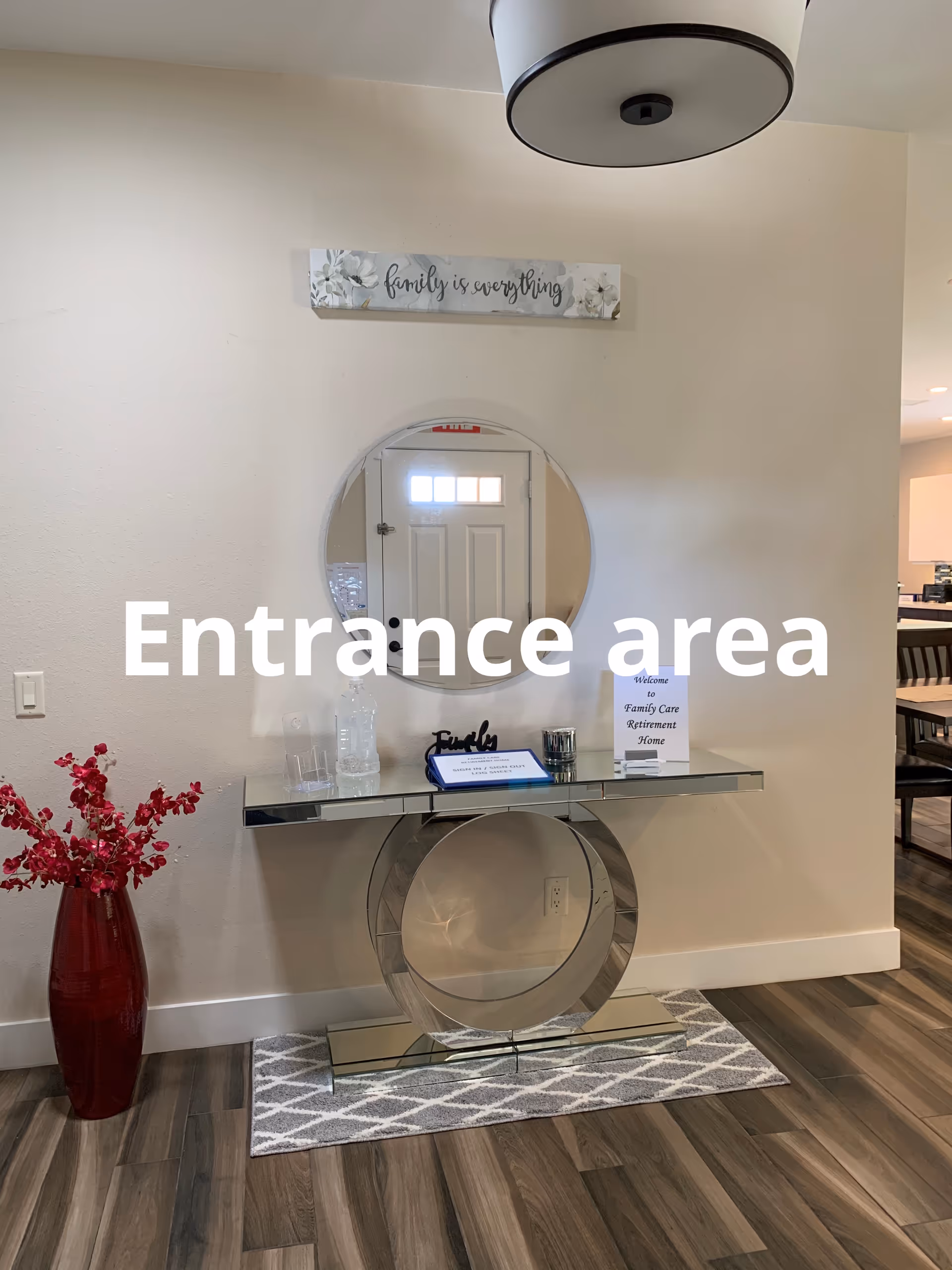 Entrance area with round mirror, glass console table, 'family is everything' sign, and red vase.