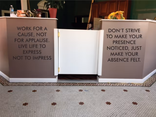 Open white gate between beige podiums with motivational quotes, tiled floor, potted plants.