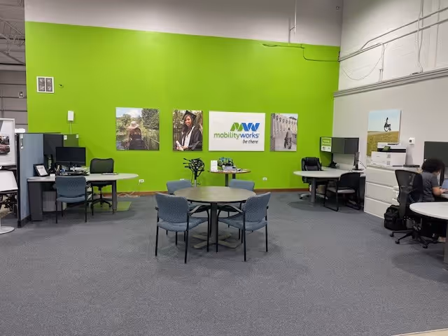 Bright interior with a lime-green wall, round table, chairs, desks, and MobilityWorks signage.