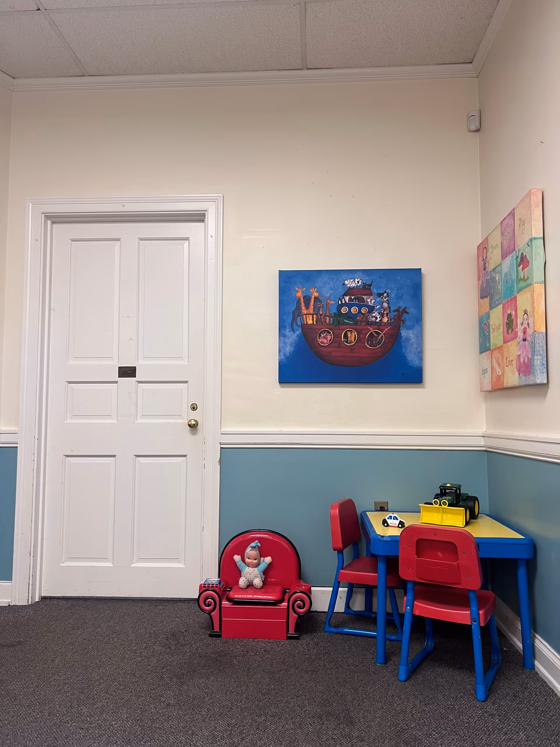 Interior play area with a small table, colorful chairs, toys, and wall art.