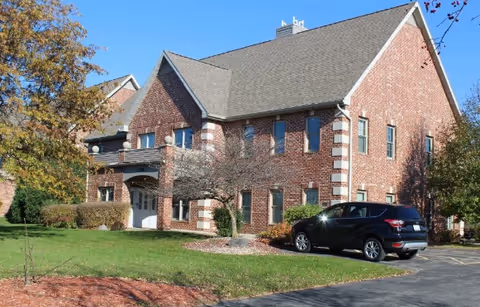 Brick senior living facility exterior with a parked black SUV and manicured landscaping.