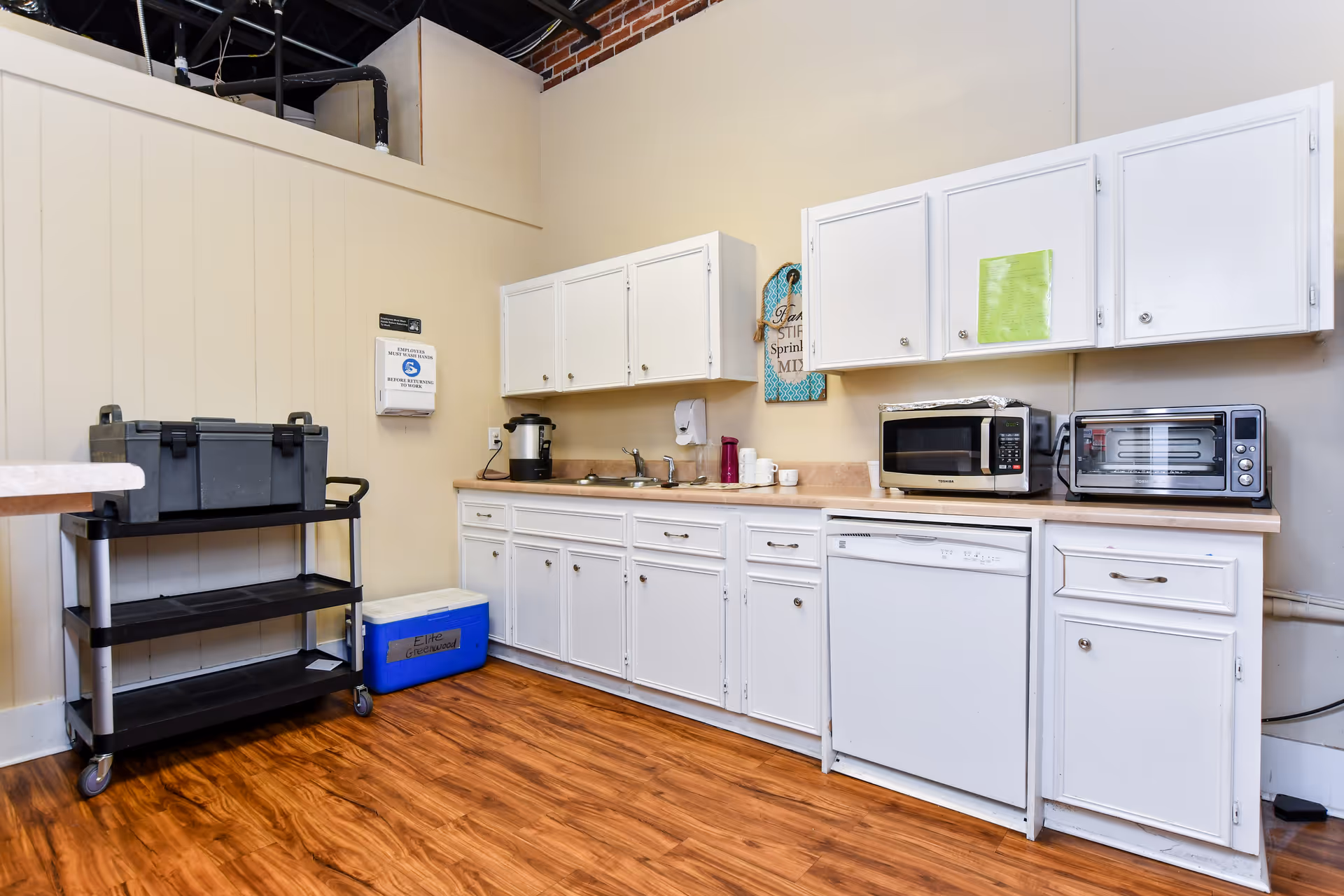 In a senior living facility kitchen, white cabinets line the counter with a cart and cooler.