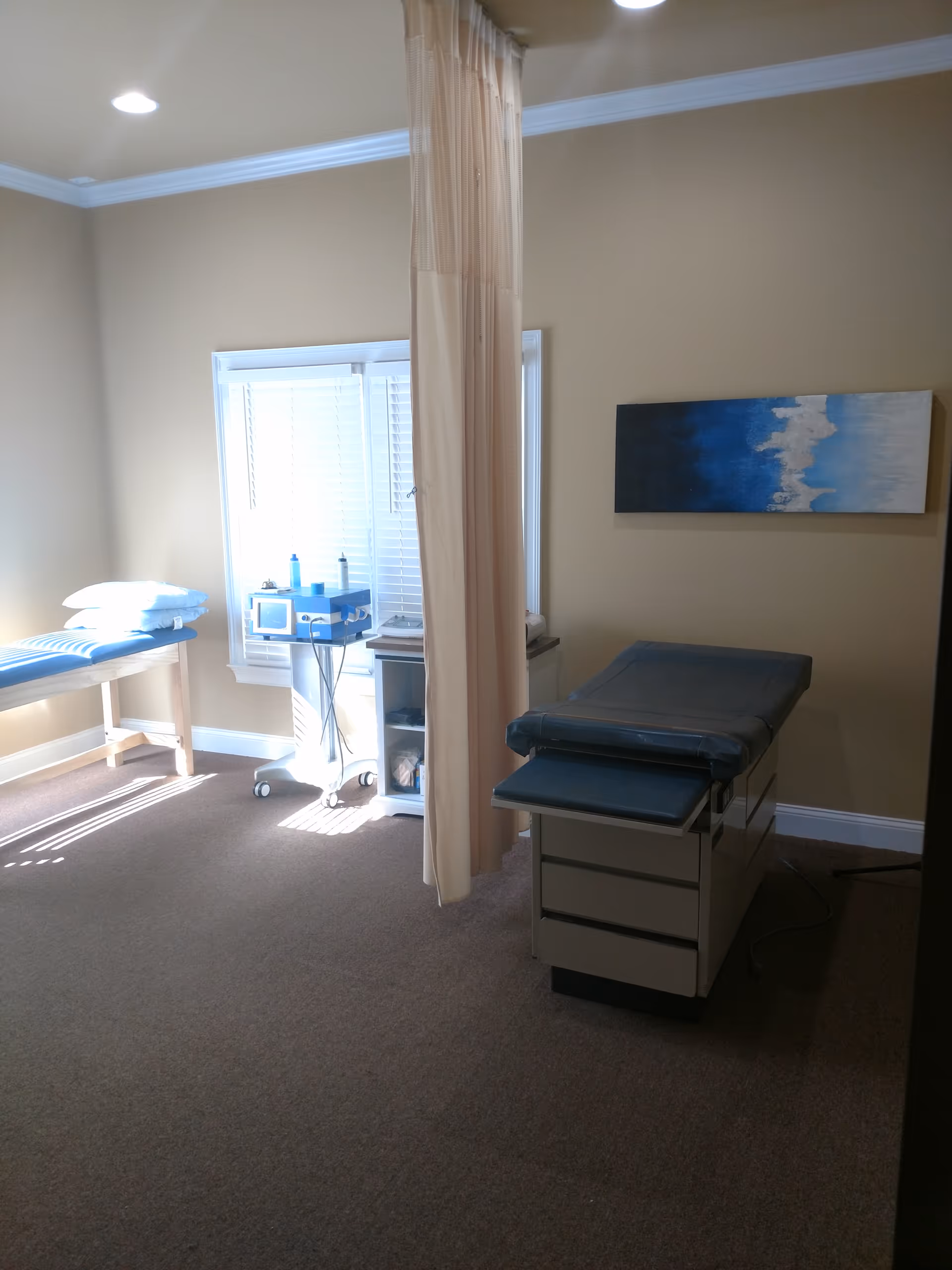 An interior treatment room with a curtain, exam bed, and medical equipment.
