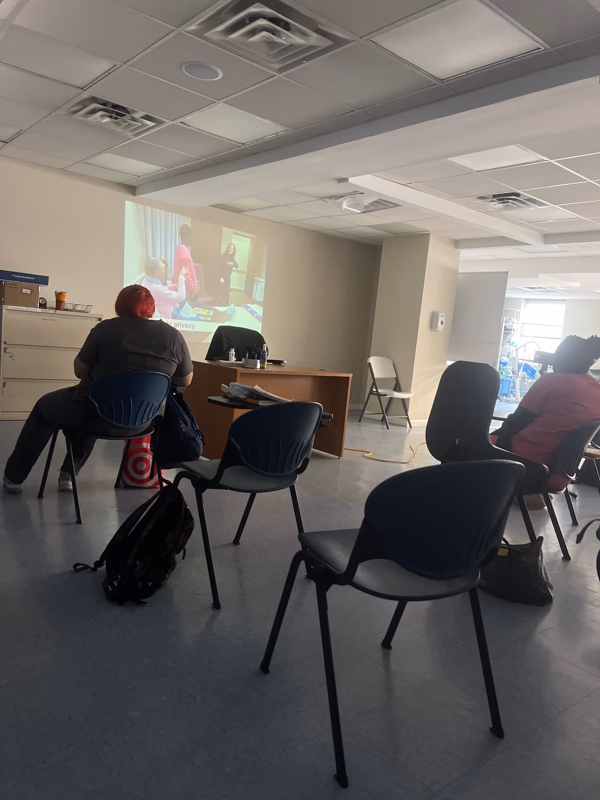 A conference room in a senior care facility with a projector screen and seated attendees.