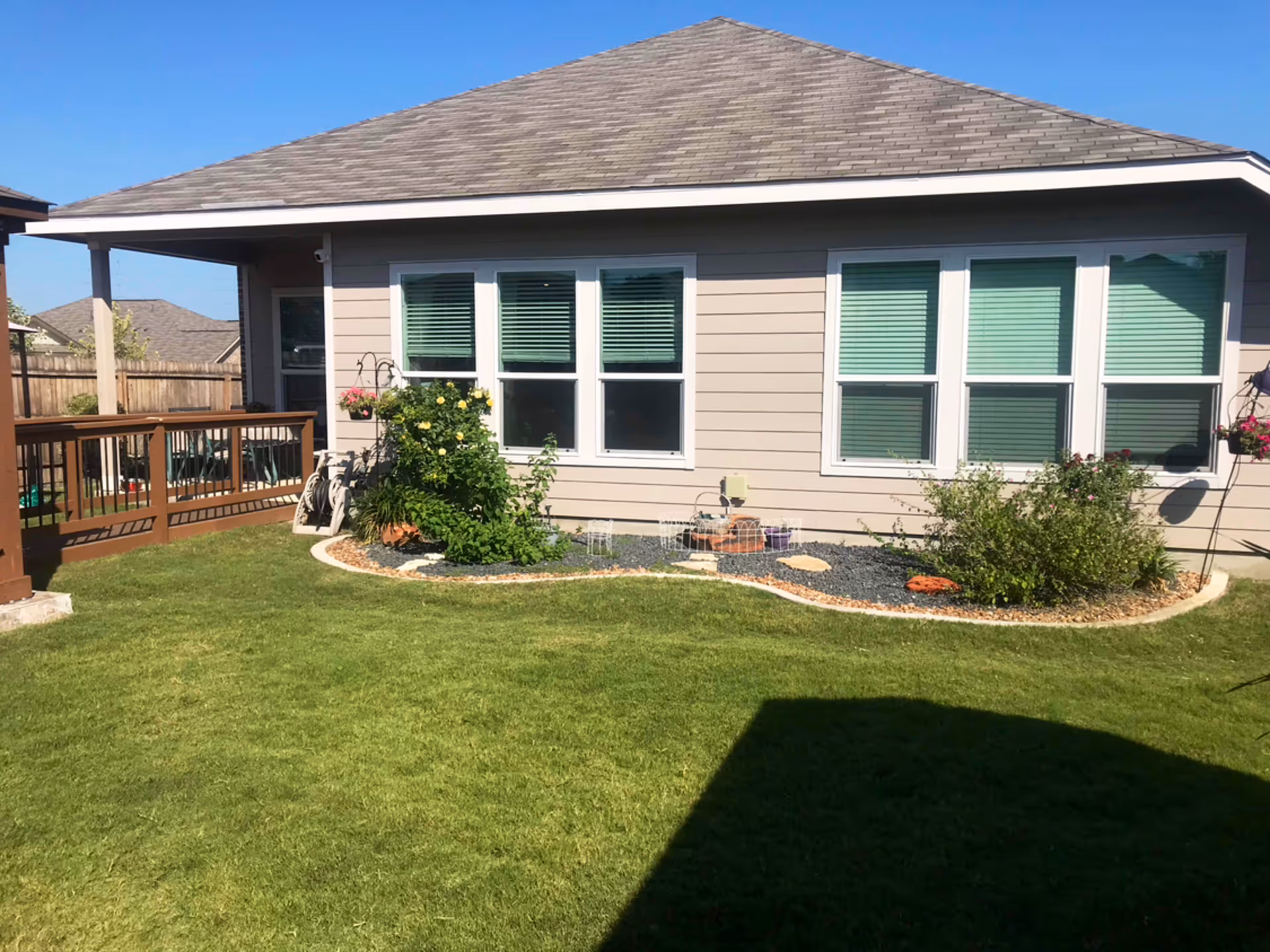 Single-story beige house with a manicured lawn, garden beds, and a wooden deck.