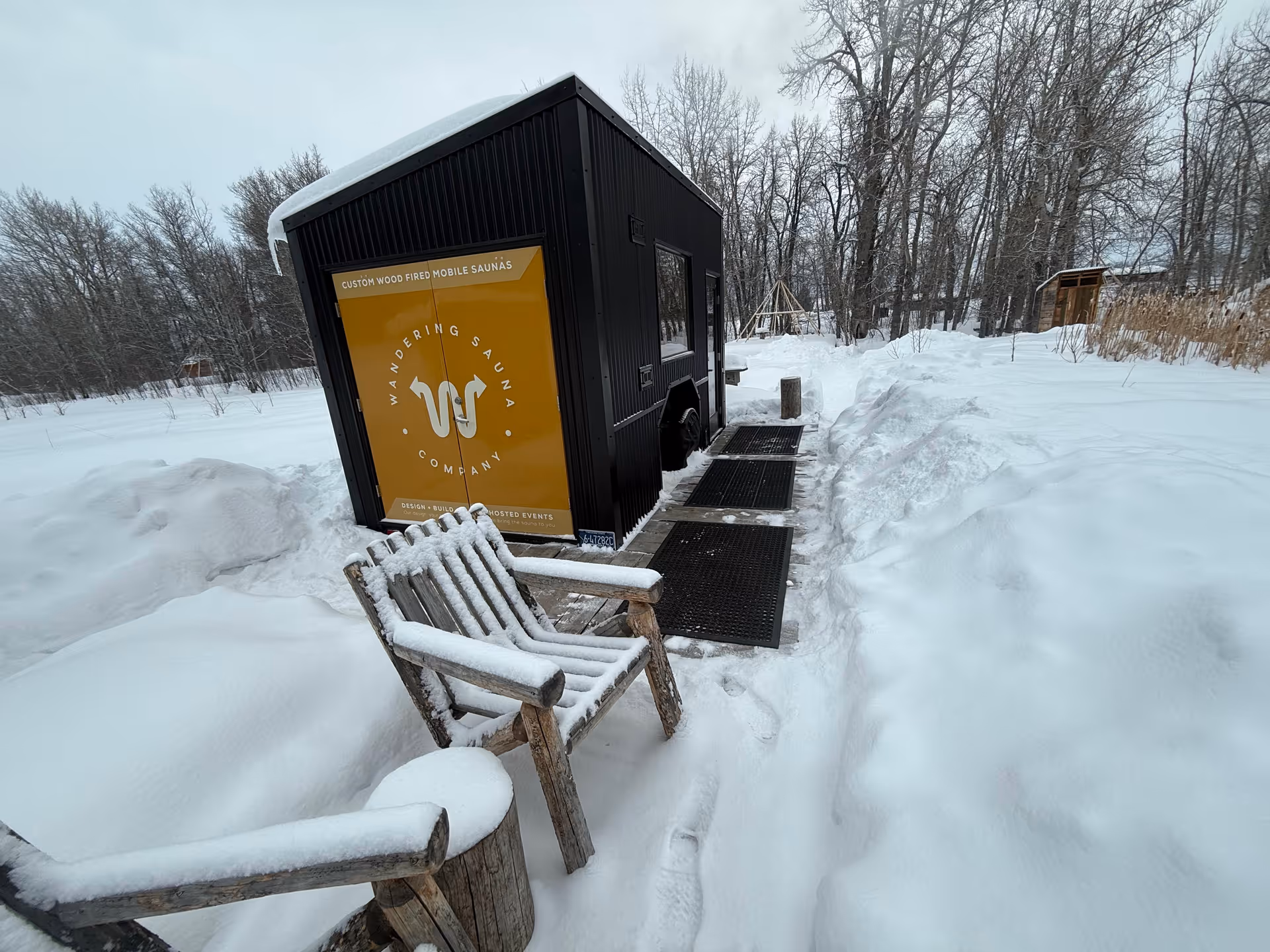 Black mobile sauna trailer with orange logo sits in a snowy outdoor setting.