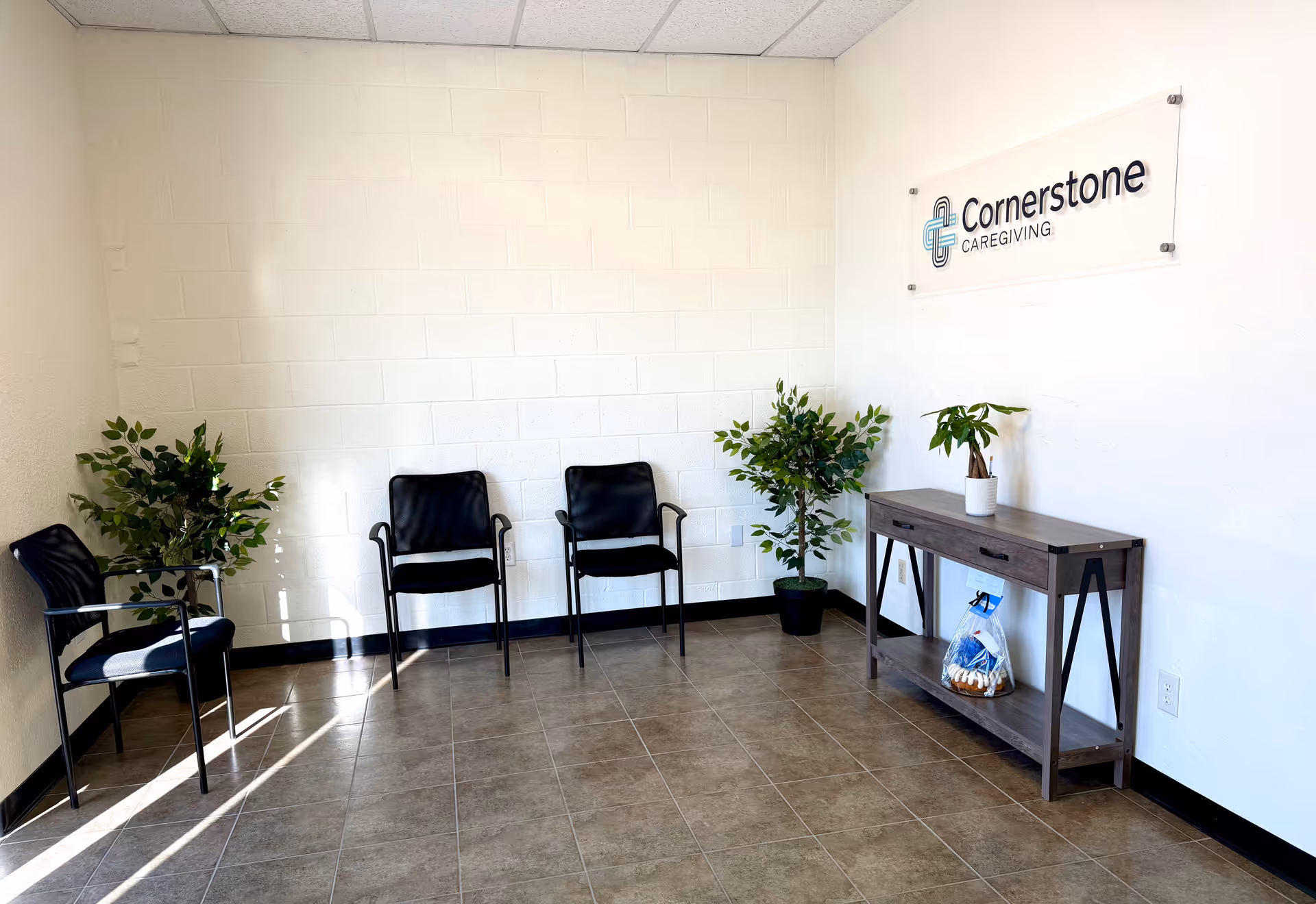 Waiting area with black chairs, plants, and a Cornerstone Caregiving sign.