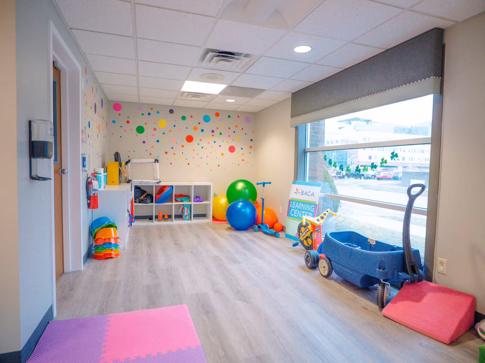 Bright playroom for therapy with colorful wall decals, shelves, and a large window.