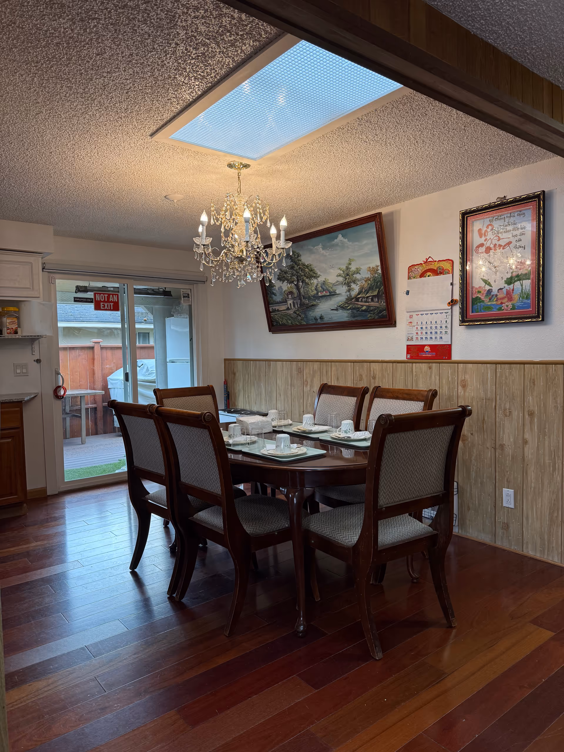 Dining room setup with a chandelier, wooden floors, and a table set for a meal.