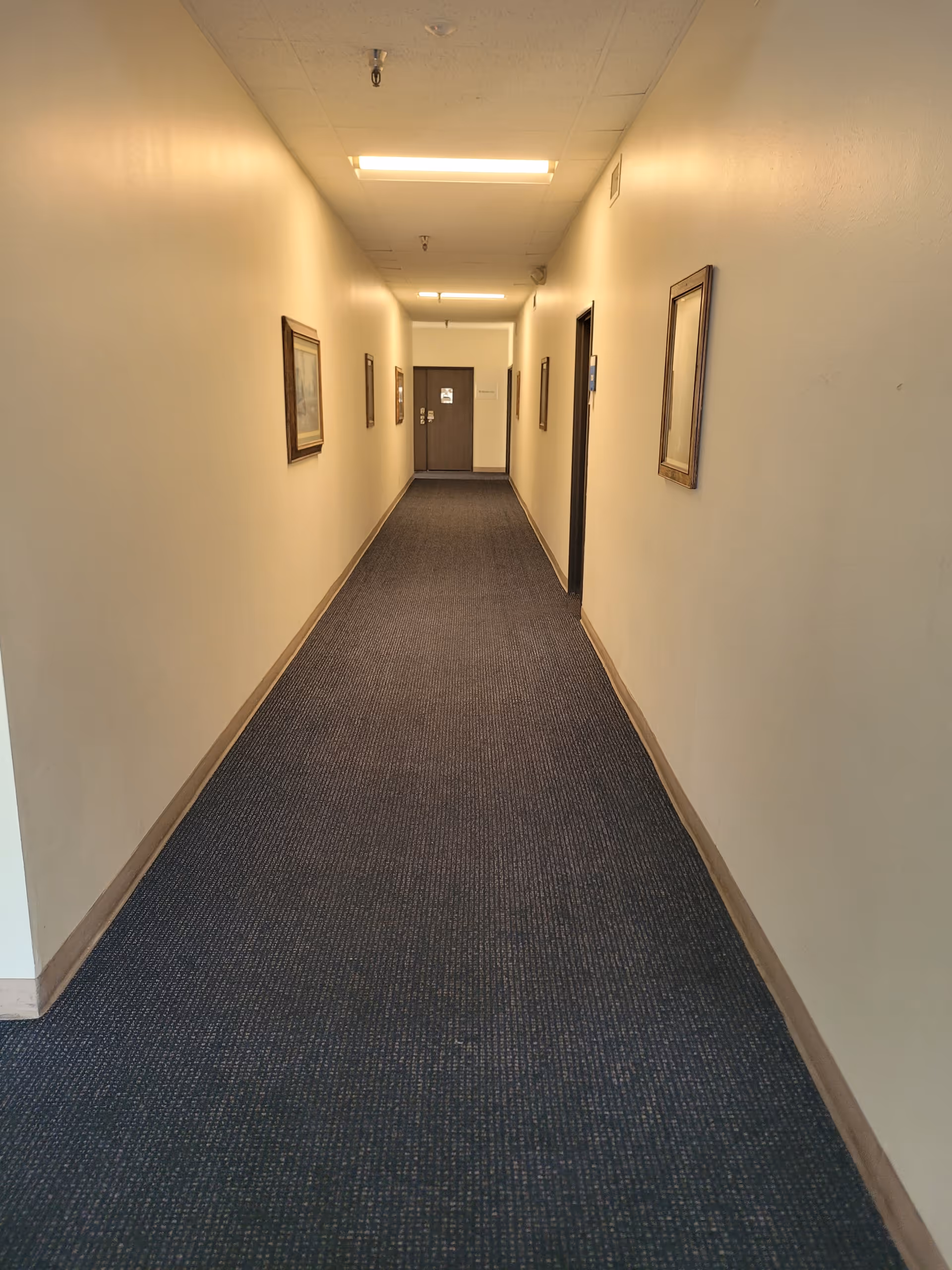 Long carpeted hallway in a senior living facility with framed wall art.