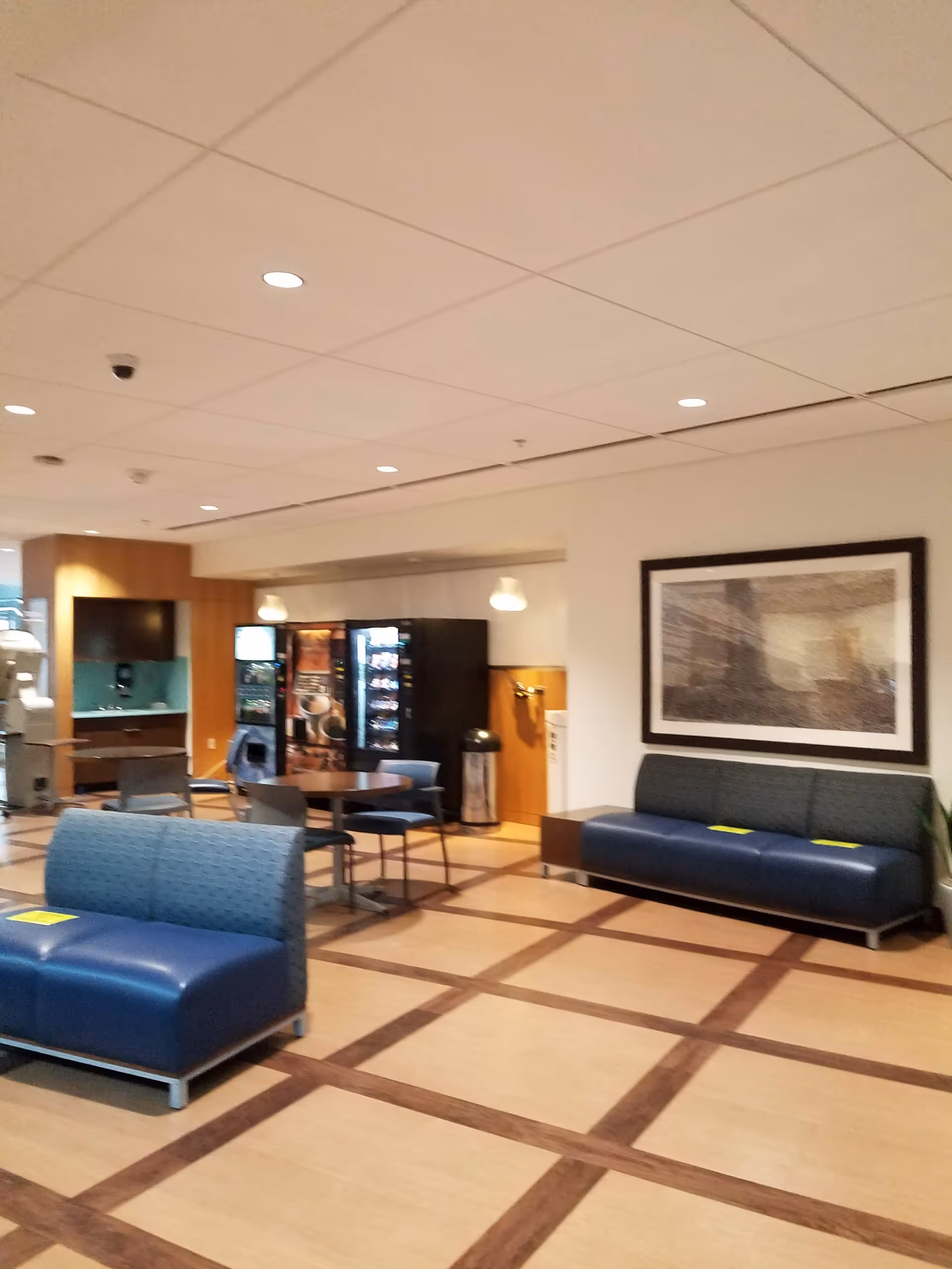 Interior lounge area with blue couches, tables, vending machines, and framed artwork.