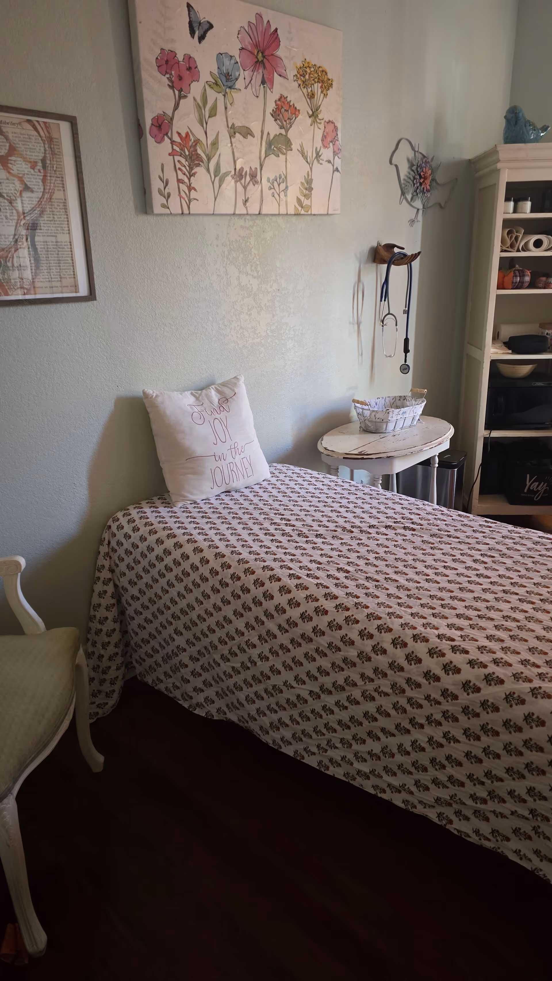 A small patient room with a bed, floral art, and medical equipment.
