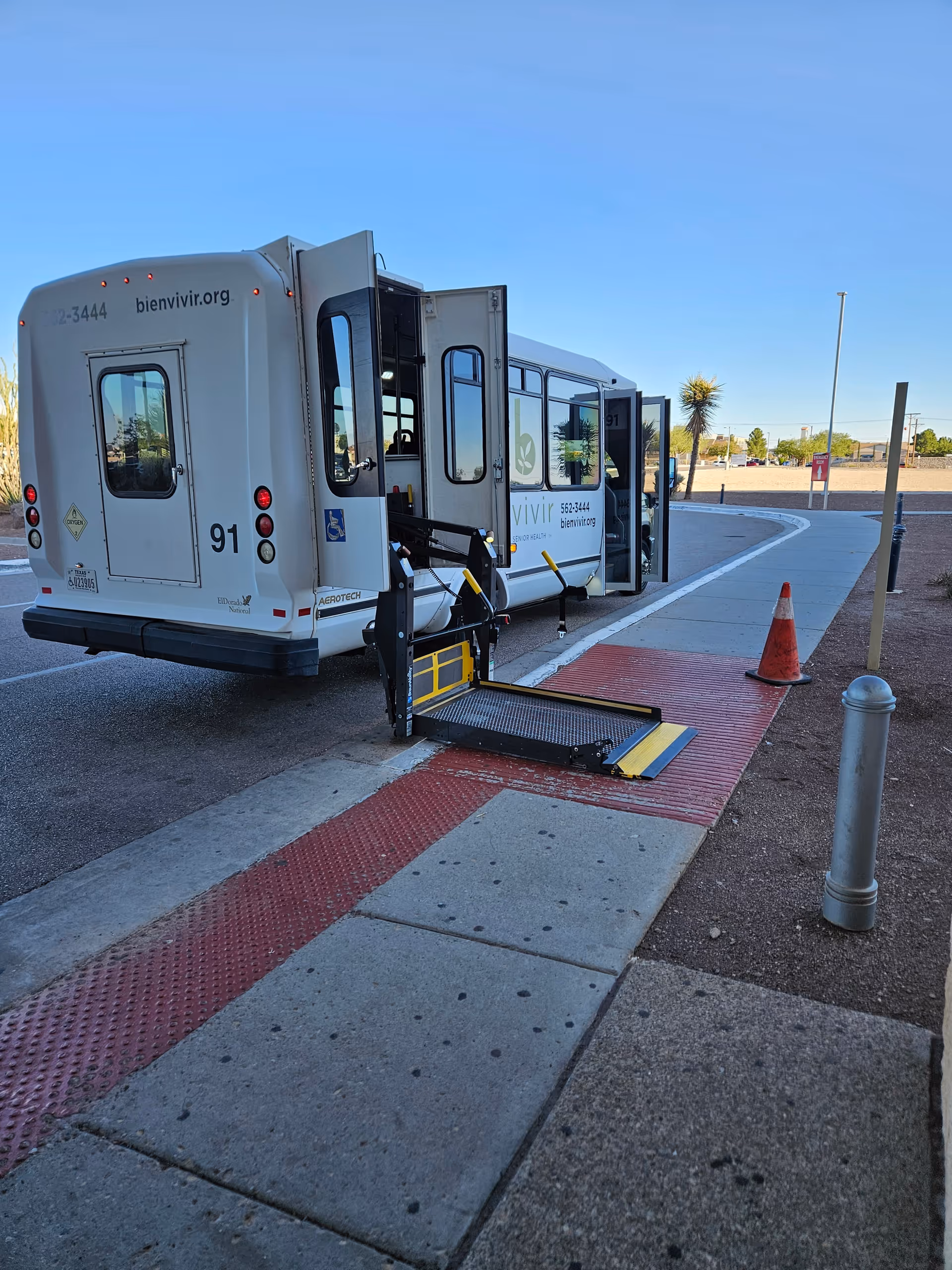 White transit bus with an extended ramp parked by a sidewalk outside.