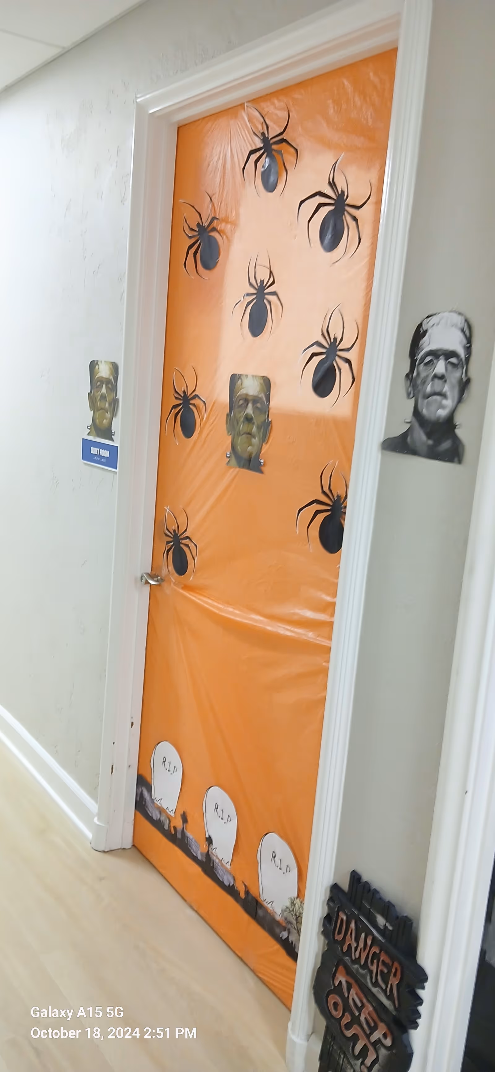 Orange Halloween door in a hallway with spider decals and eerie face cutouts.