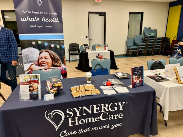 Indoor promotional table for Synergy HomeCare with brochures and banners inside.