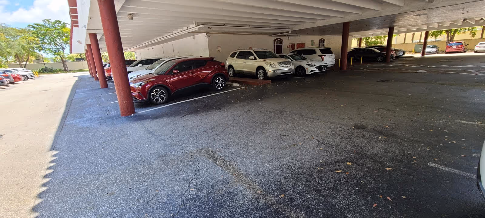 Covered parking area under a building with multiple parked cars.