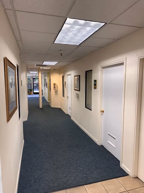 Interior corridor of a senior living facility with doors, artwork, and blue carpet.