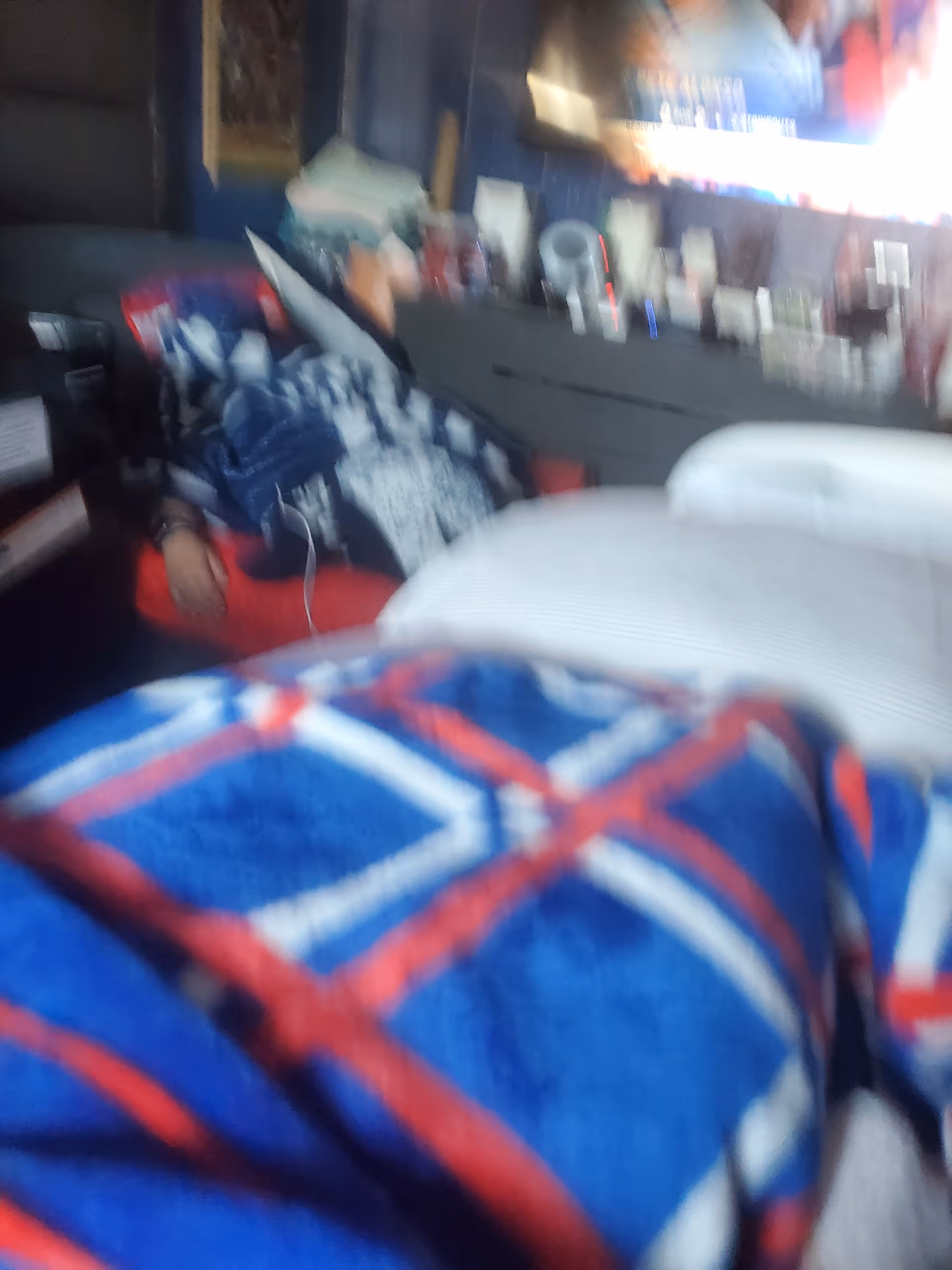 Blurry bedroom scene with a patterned blanket and cluttered dresser in a home care room.