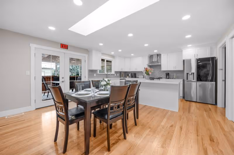 Bright open dining area with a wooden table, chairs, and a modern white kitchen.