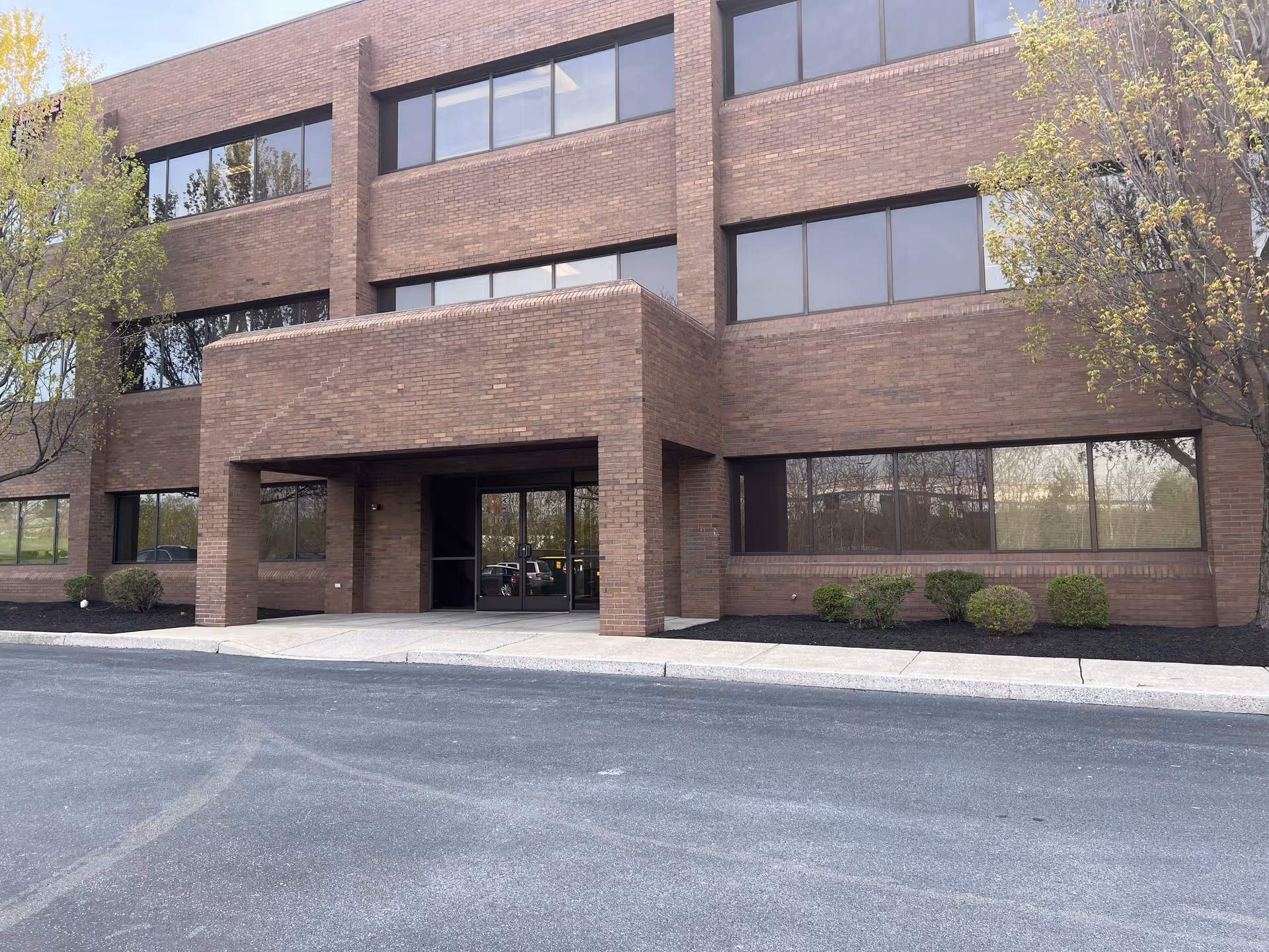 Brick multi-story office building with a glass entrance and manicured shrubs along the front.