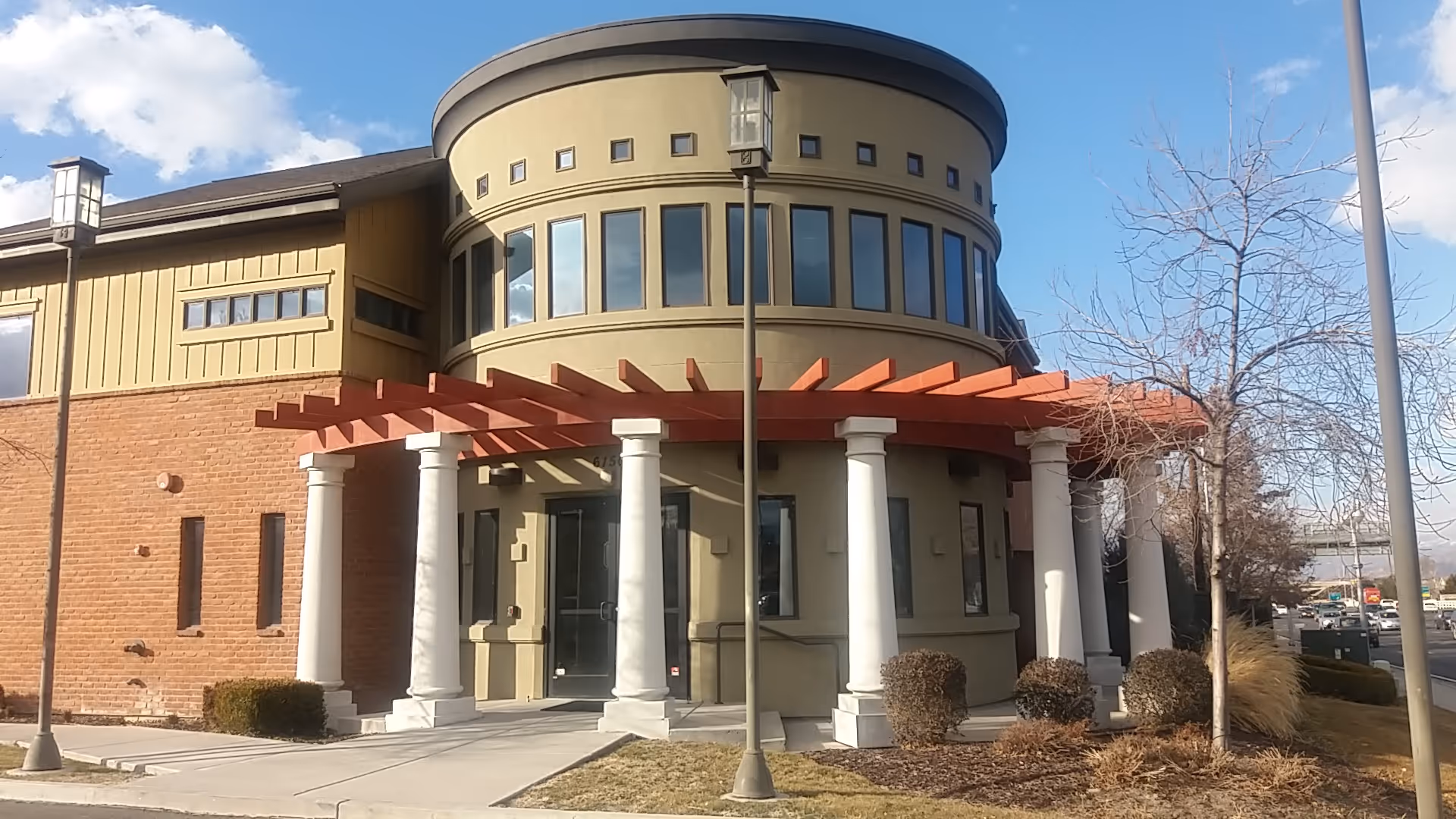Exterior view of a modern senior living facility with a circular turret and red pergola.
